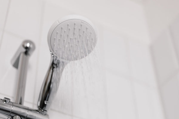 Water streaming from a chrome and white shower head in a clean white tiled home bathroom