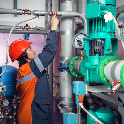 Facilities operator adjusting a valve on circulation pumps in a building mechanical room