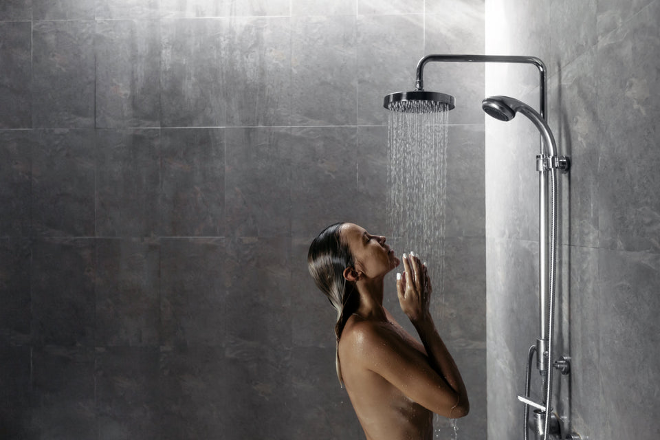 Woman showering under a rainfall showerhead in a gray tiled bathroom