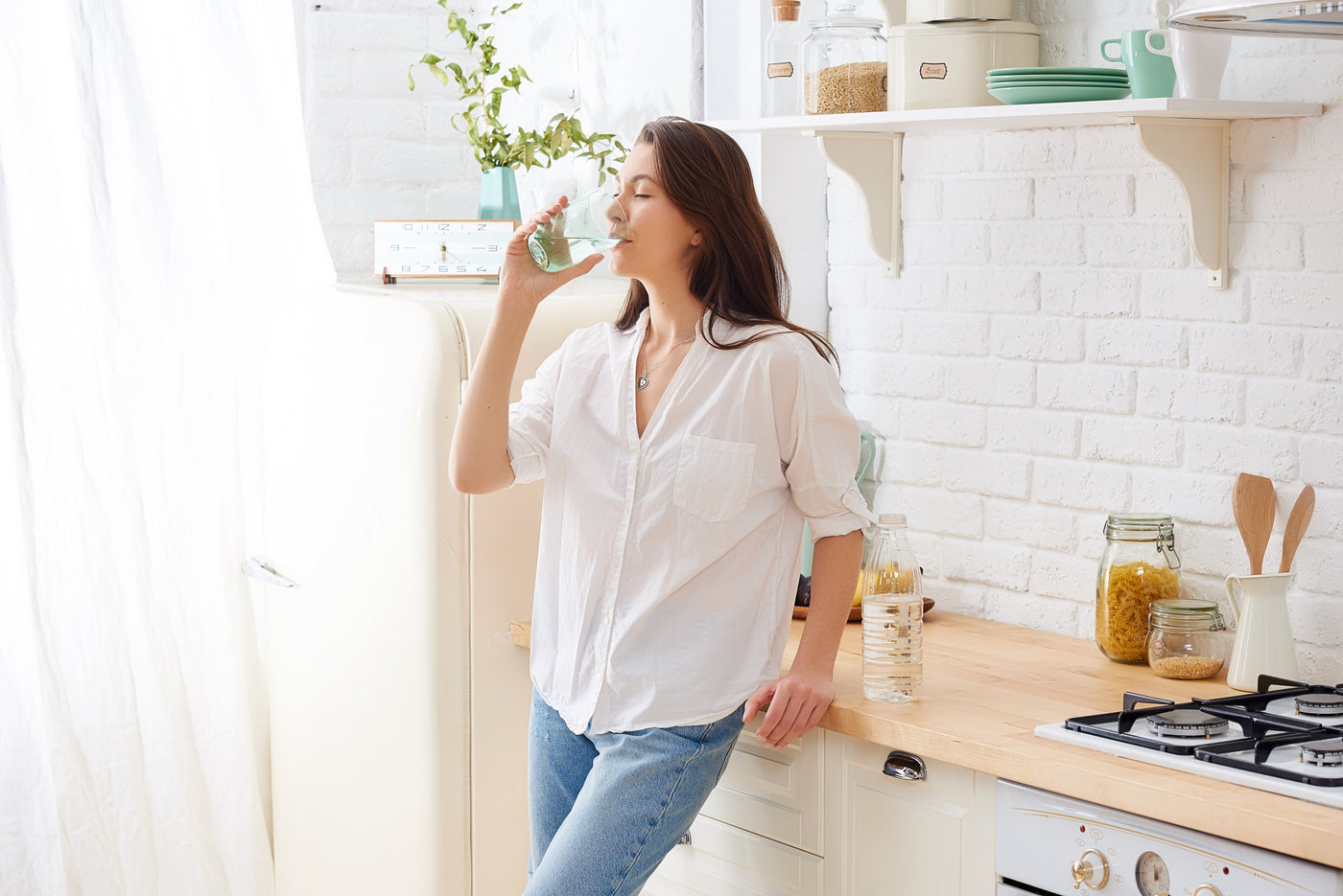 Woman drinking a clear glass of water in a bright modern kitchen