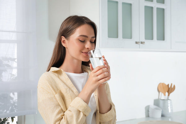 Woman in a bright kitchen sipping a glass of clean filtered water