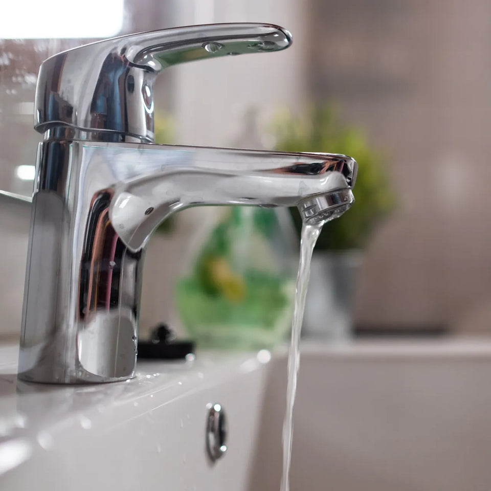Chrome bathroom faucet running a clear stream of water over a white sink
