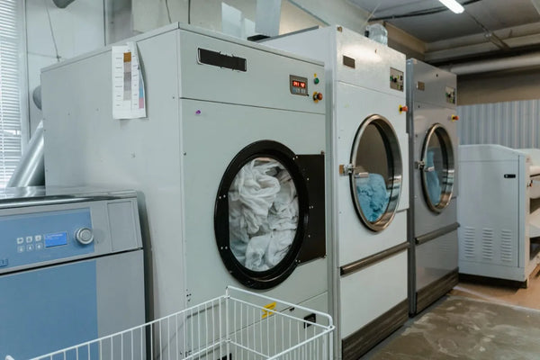 Industrial washer extractors loaded with white and blue linen in an on premise commercial laundry, with a flatwork ironer at right