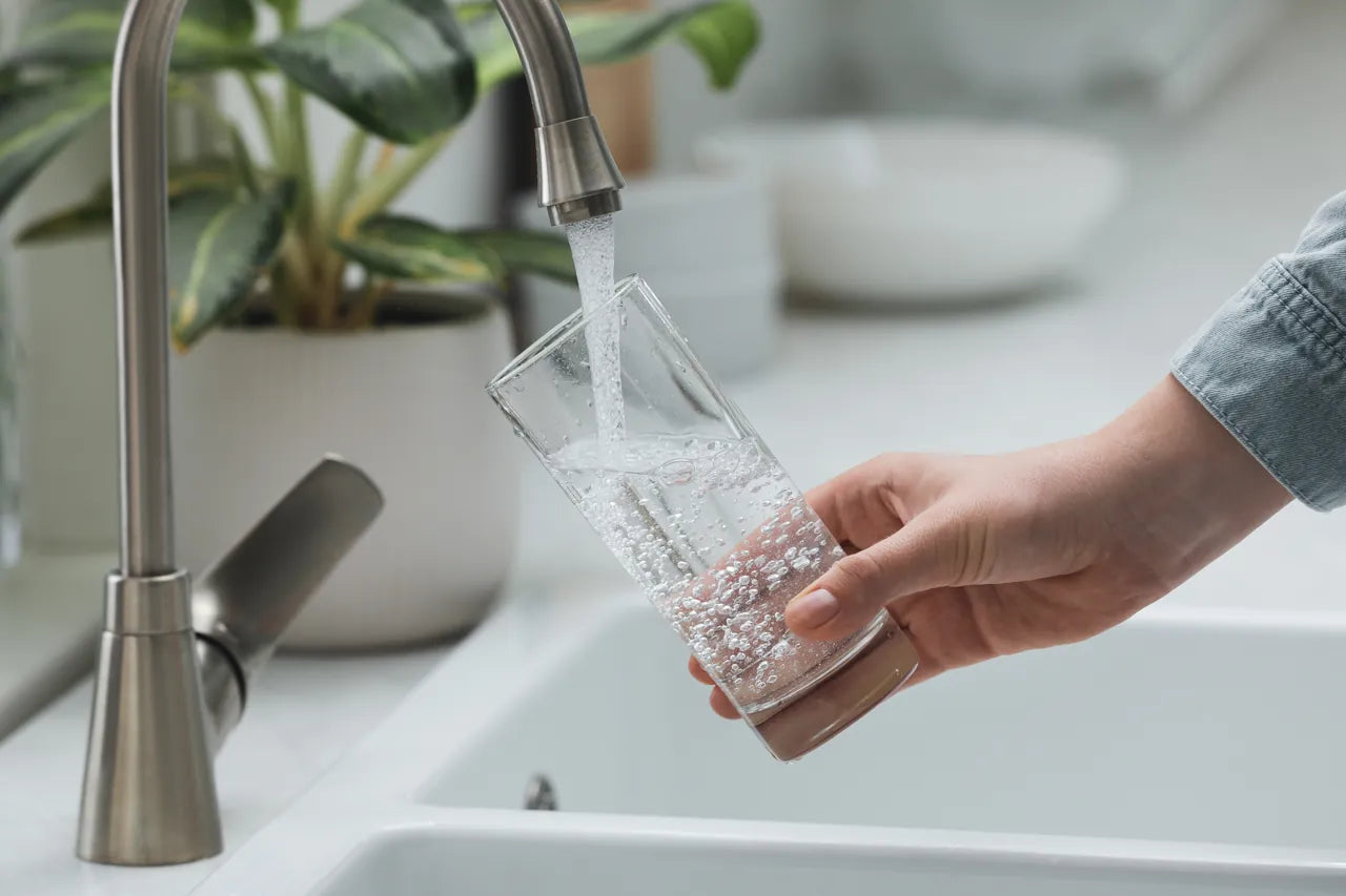 Hand filling a drinking glass with water at a chrome kitchen faucet in a bright kitchen