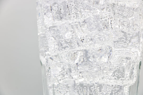 Close-up of a tall glass filled with ice cubes and clear sparkling carbonated water with rising bubbles