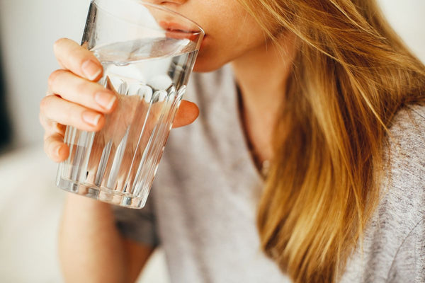 Woman drinking a glass of water indoors, a common moment when stomach discomfort can strike