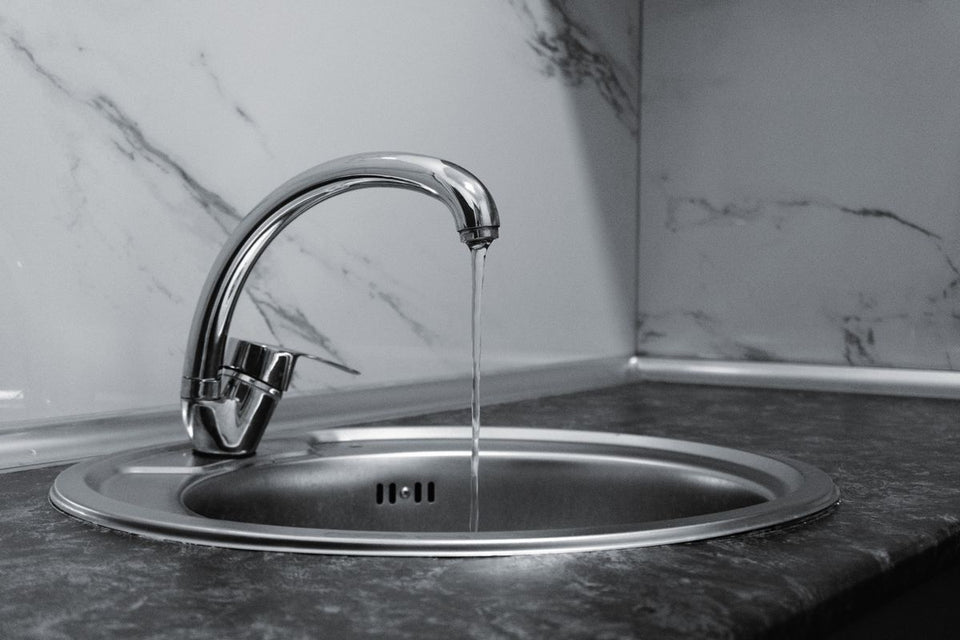 Stainless steel kitchen faucet running a thin stream of water into a round sink, shown in black and white