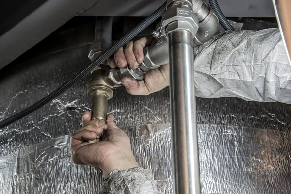 A person using a wrench to connect brass and stainless steel water supply pipes and a shutoff valve during a home water softener installation