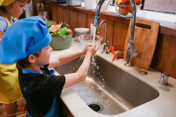 Children washing hands at a kitchen sink faucet in a bright home kitchen