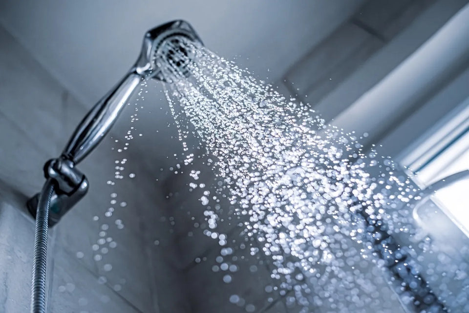 Chrome showerhead spraying water in a tiled shower, the warm damp environment where pink mold bacteria form