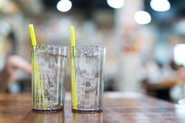 Two glasses of clear ice water with straws on a wooden table