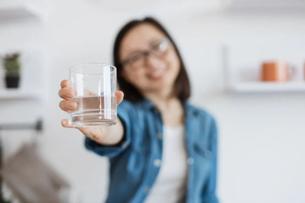 Smiling woman in denim holding out a clear glass of water
