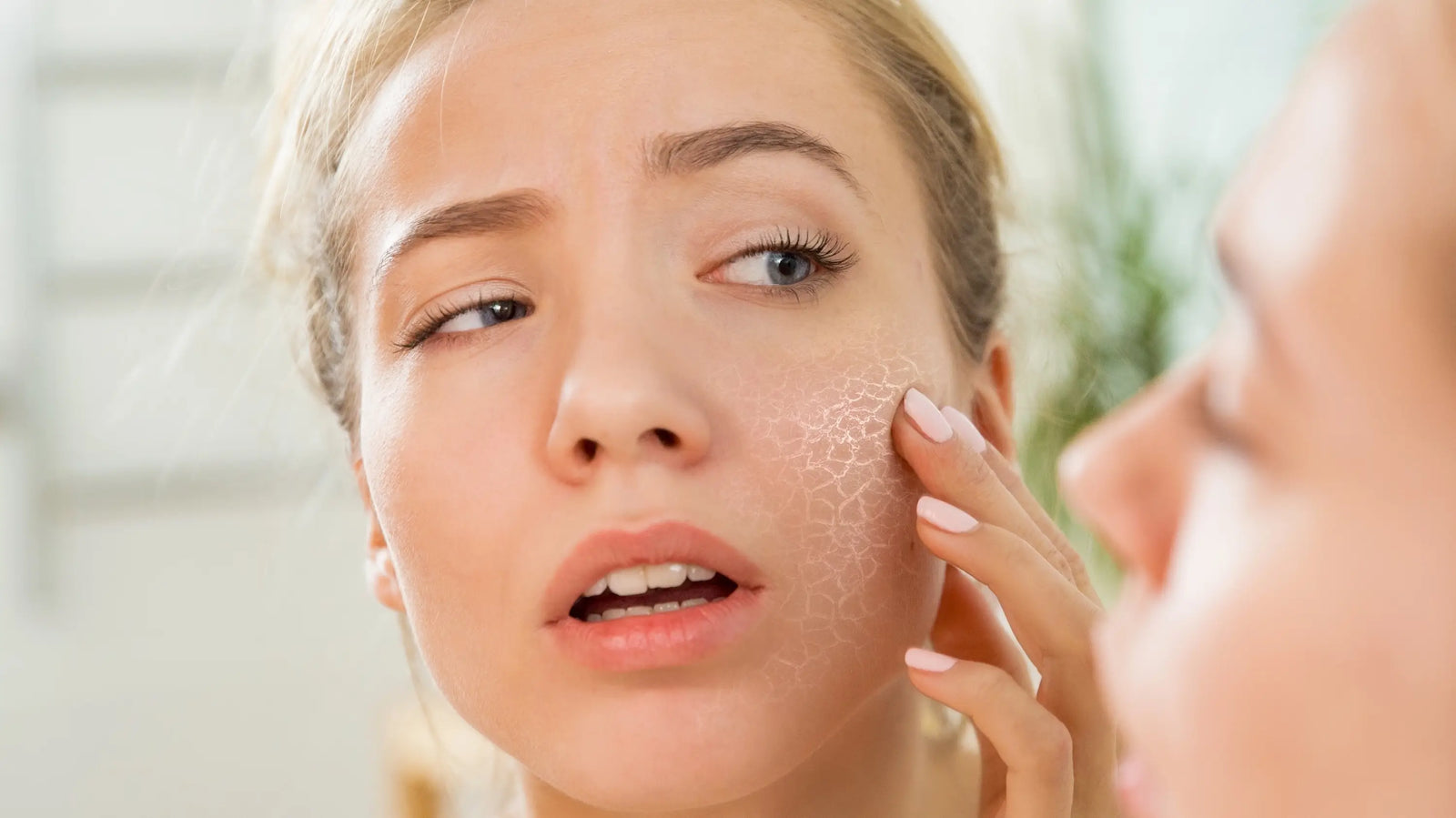 woman looking at her skin in the mirror with highlight on cheek for dry skin caused by hard water